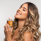 Mujer con cabello ondulado sosteniendo el perfume capilar Click Hair de miel 100 ml junto al rostro