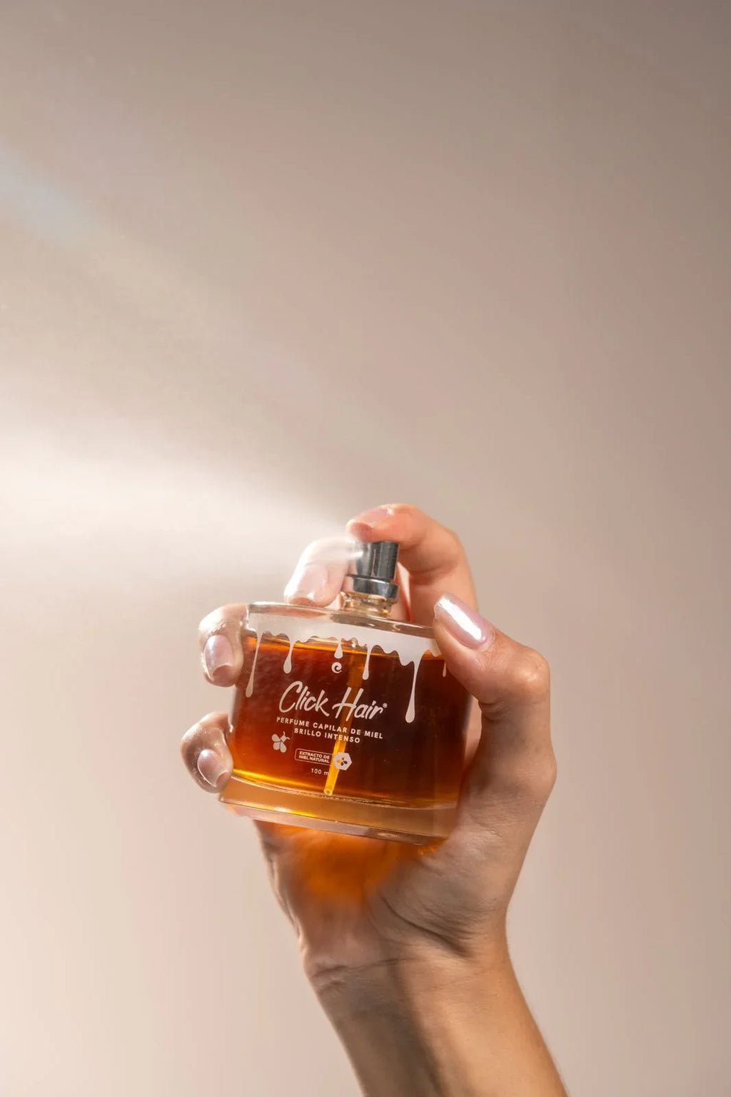 Perfume capilar Click Hair de miel 100 ml sostenido en una mano, frasco dorado con tapa rosa