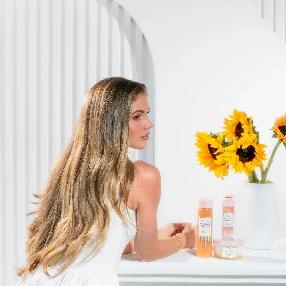 Mujer de cabello largo y ondulado junto al kit de miel Click Hair y un florero con girasoles.