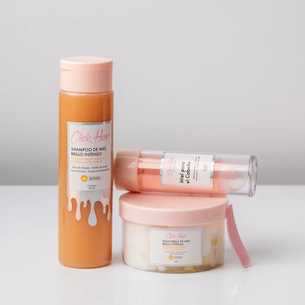 Shampoo de miel Click Hair junto a mascarilla con espátula y frasco de miel para el cabello apoyado sobre la tapa.